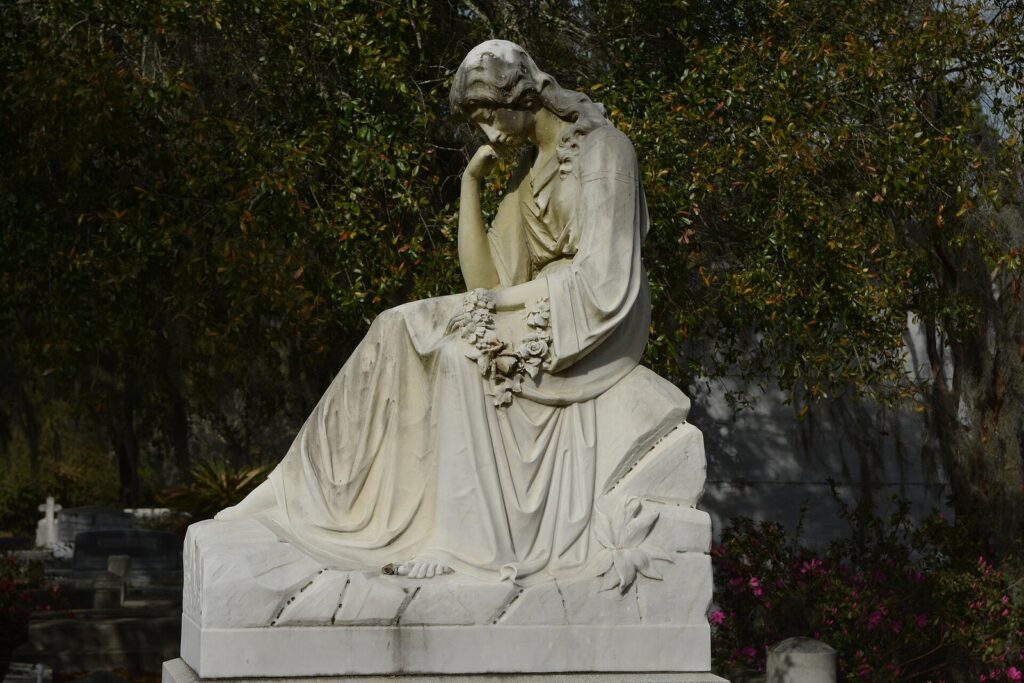 A white marble statue of a seated mourning woman among the graves of Bonaventure Cemetery