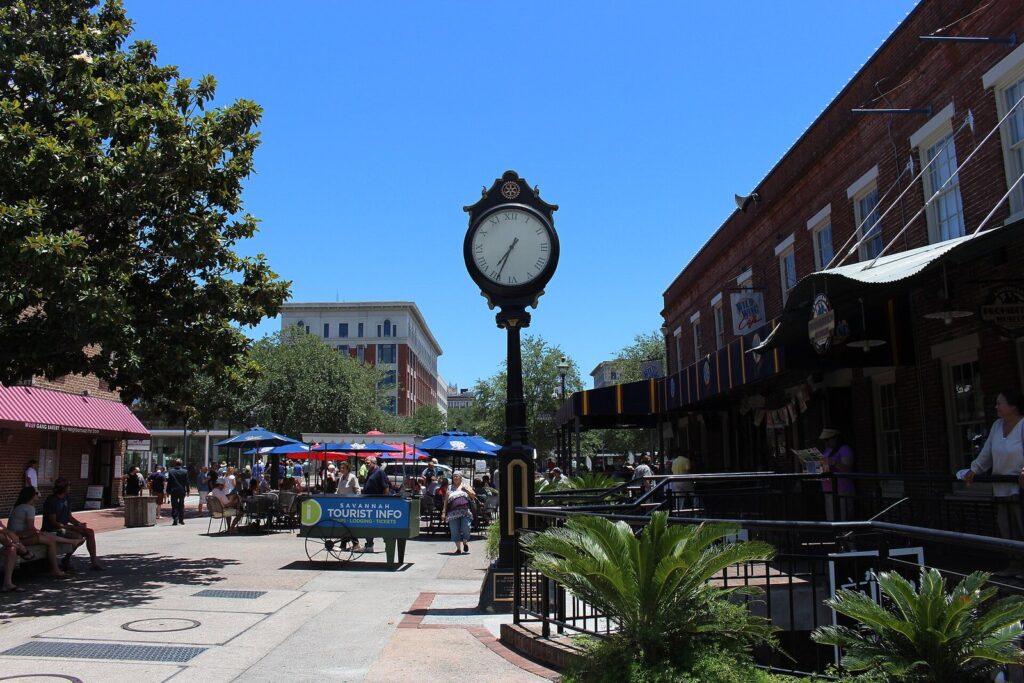 A black street clock and outdoor restaurant tables in the pedestrian courtyard of City Market in Savannah