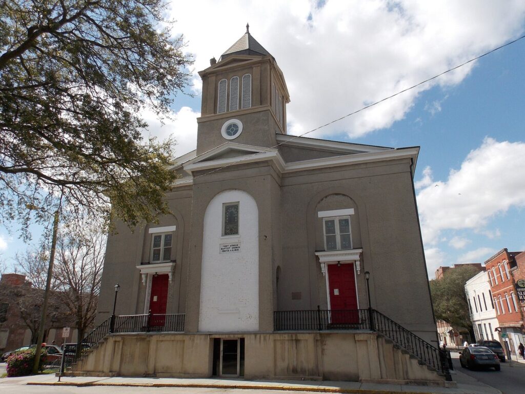 The gray stucco front of First African Baptist Church in Savannah, with its square bell tower and red doors