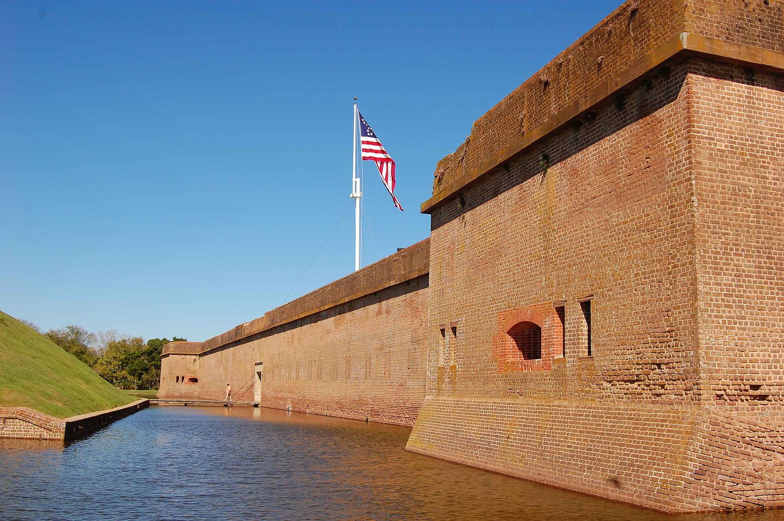 The high brick walls of Fort Pulaski rising from its water-filled moat under a blue sky, with a US flag flying