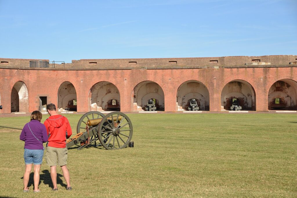 Two visitors look at a field cannon on the parade ground inside the brick walls of Fort Pulaski