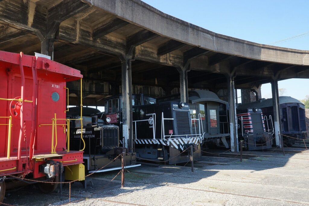 Locomotives and a red caboose parked under the curved roundhouse at the Georgia State Railroad Museum