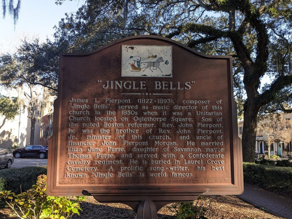 A brown historical marker titled Jingle Bells in Troup Square, Savannah, with live oaks behind it