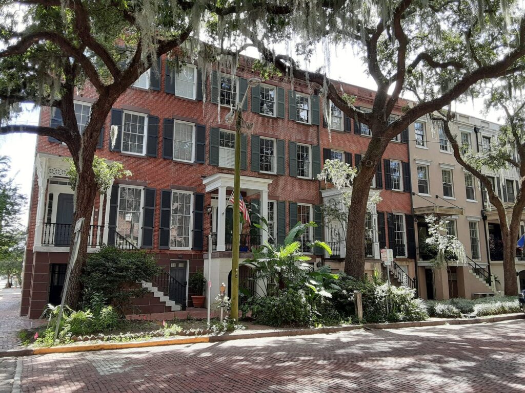 Brick row houses with black shutters under live oaks on Jones Street in Savannah