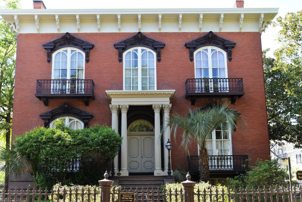 The red brick Mercer Williams House on Monterey Square, with arched windows, iron balconies and a white columned entrance