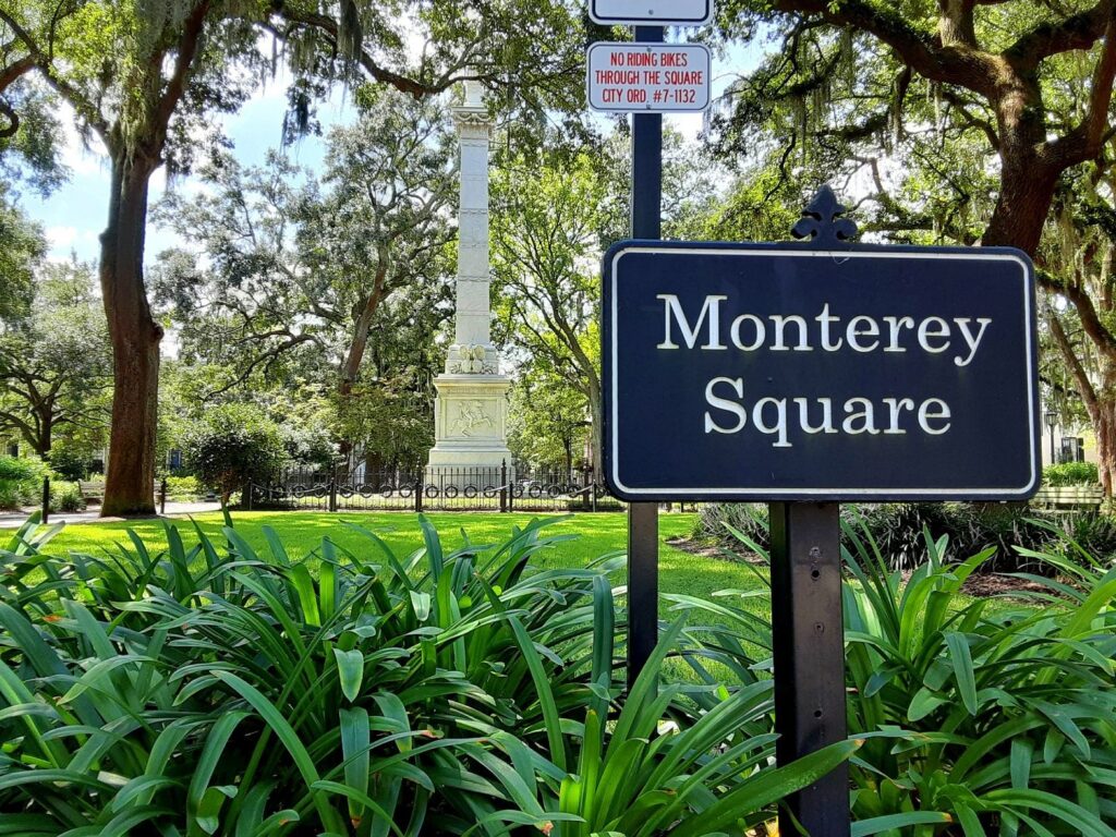 The Monterey Square sign in front of green lawn, live oaks and the Pulaski monument in Savannah
