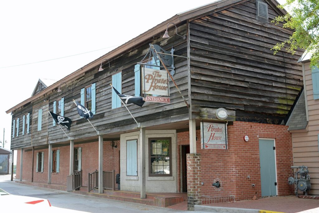The weathered wooden upper story and brick ground floor of The Pirates' House in Savannah, with pirate flags over the entrance