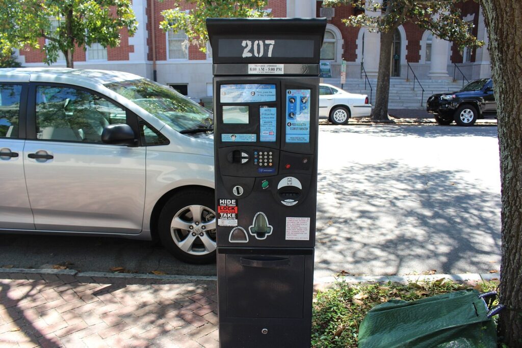 A pay-by-space parking meter on a brick sidewalk beside parked cars on Bull Street in Savannah
