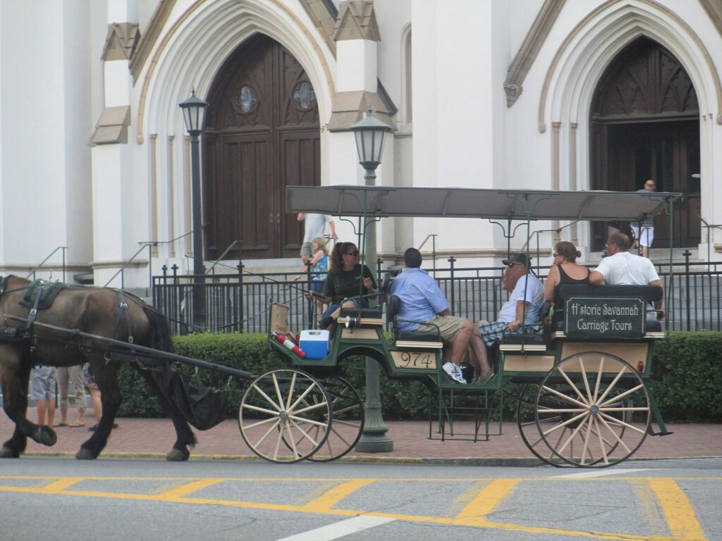Best Savannah tours: a horse-drawn carriage tour with passengers passing the Cathedral Basilica of St. John the Baptist