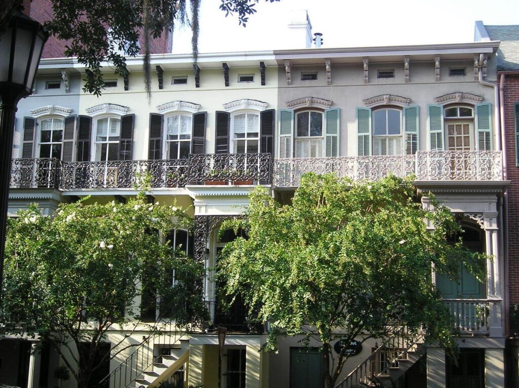 Savannah Georgia travel guide: a pale historic townhouse with cast-iron balconies behind leafy trees in the Historic District