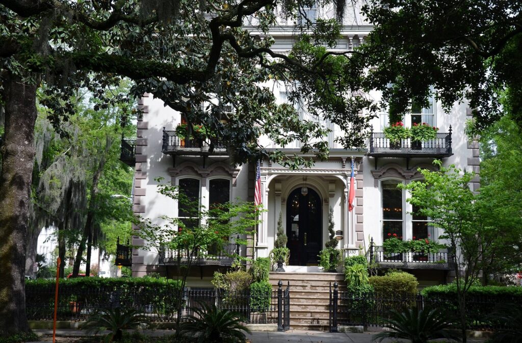 An ornate white historic mansion with iron balconies behind live oaks in Savannah's Historic District