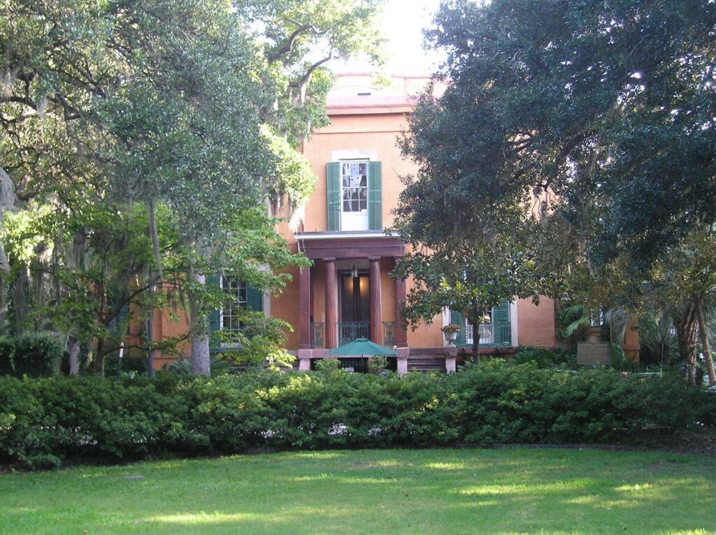 A salmon-colored historic house seen through live oaks across Madison Square in Savannah