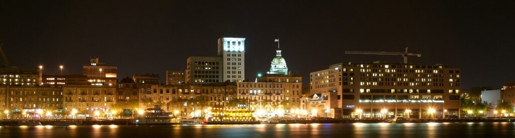 Downtown Savannah's riverfront lit up at night, with City Hall's gold dome among the buildings along the river