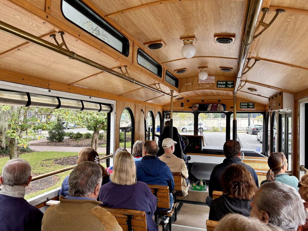 Passengers seated on wooden benches inside a Savannah trolley tour vehicle, looking out at a square