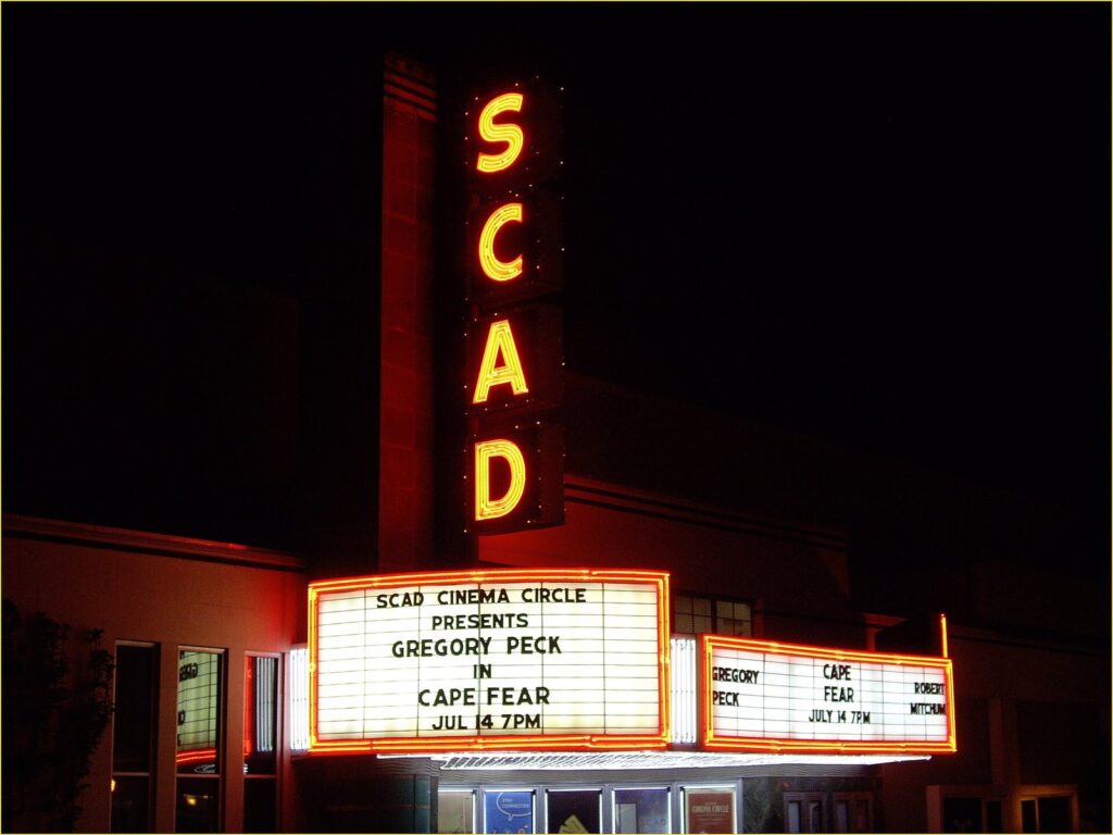 The glowing SCAD sign and lit marquee of the Trustees Theater on Broughton Street at night