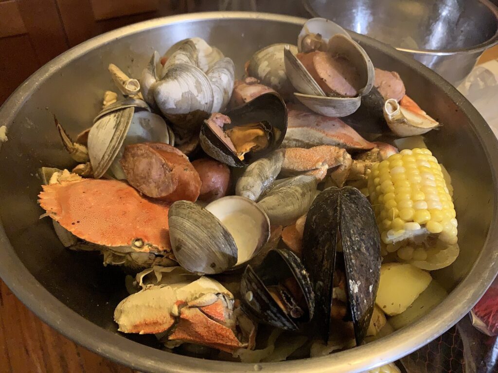 A metal bowl of seafood boil with crab, clams, mussels, sausage, corn and potatoes