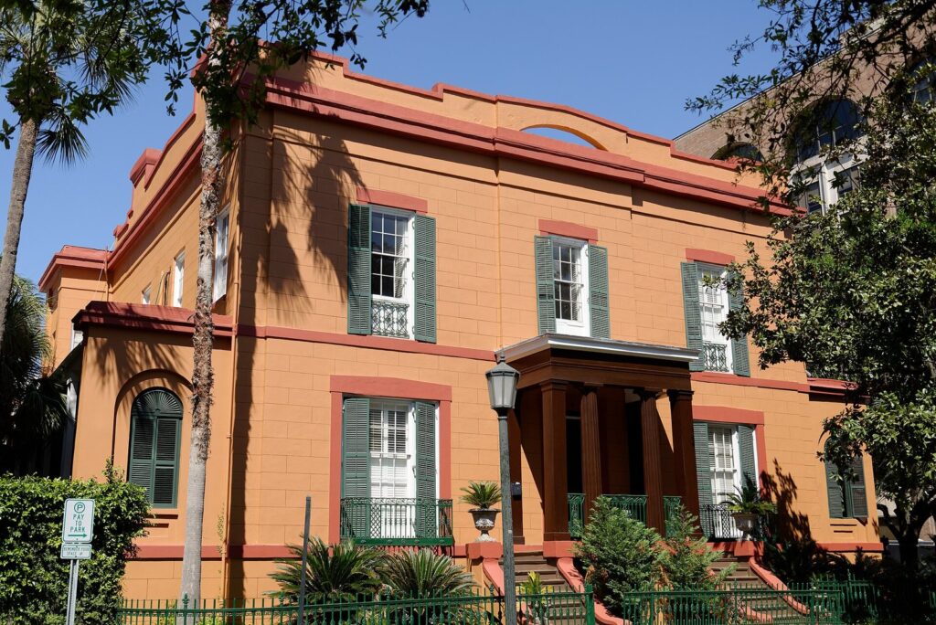 The ochre-painted Sorrel-Weed House in Savannah, with green shutters, red trim and palm trees in front