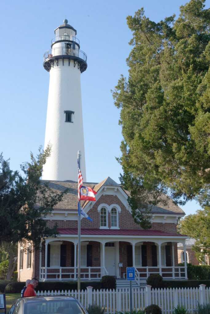 The white St. Simons Island lighthouse rising behind the brick keeper's dwelling, now a museum