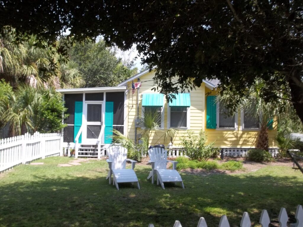 A yellow beach cottage with teal shutters and a white picket fence on Tybee Island