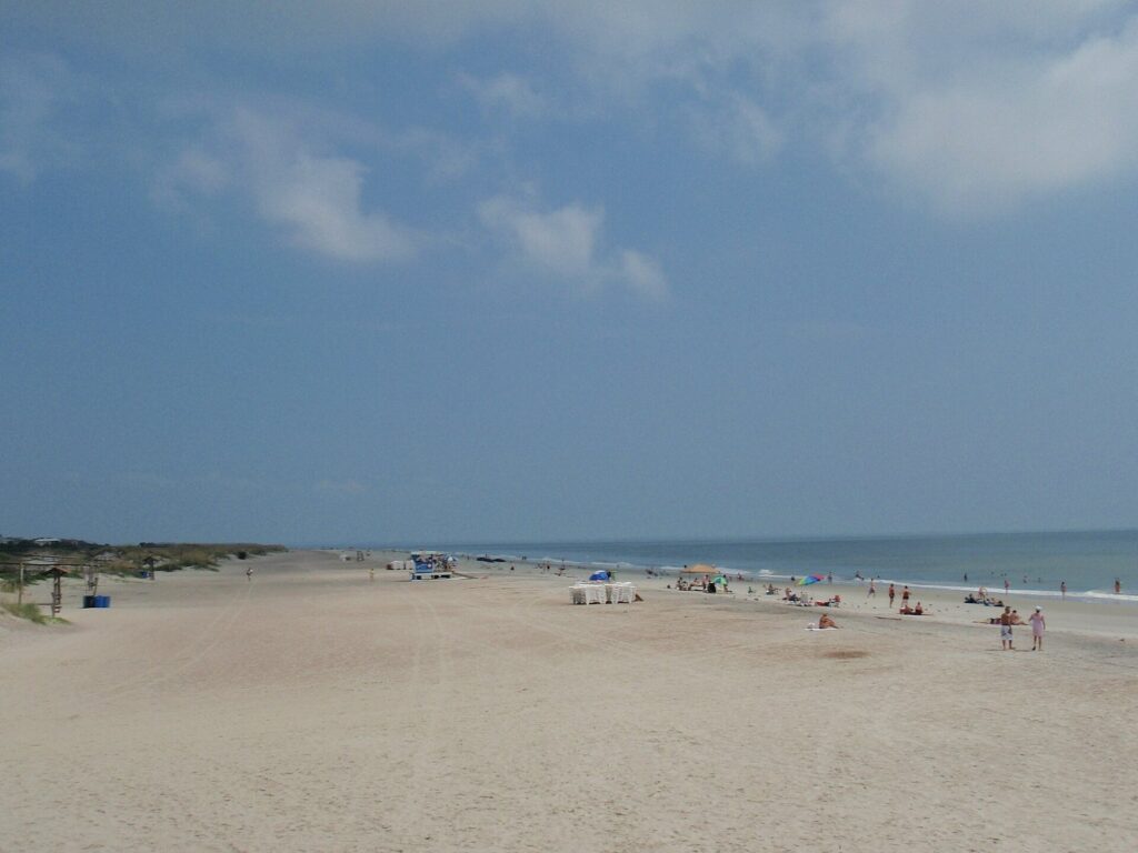 A wide sandy beach on Tybee Island with scattered umbrellas and swimmers under a cloudy sky