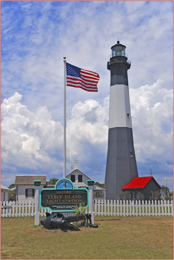 The black and white Tybee Island Light Station behind its fence and welcome sign