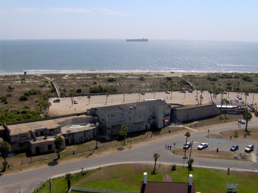 An elevated view over Tybee's North Beach area, with dunes, a parking lot, old concrete buildings and the Atlantic beyond