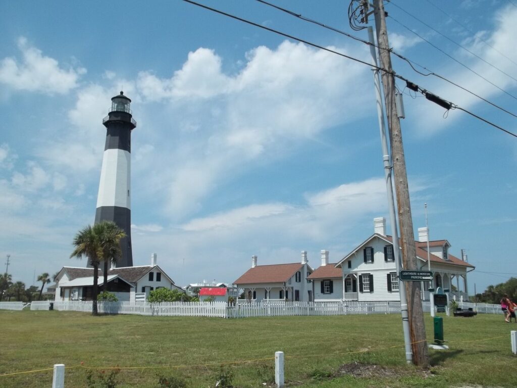 The black and white Tybee Island lighthouse behind white keepers' cottages and a picket fence