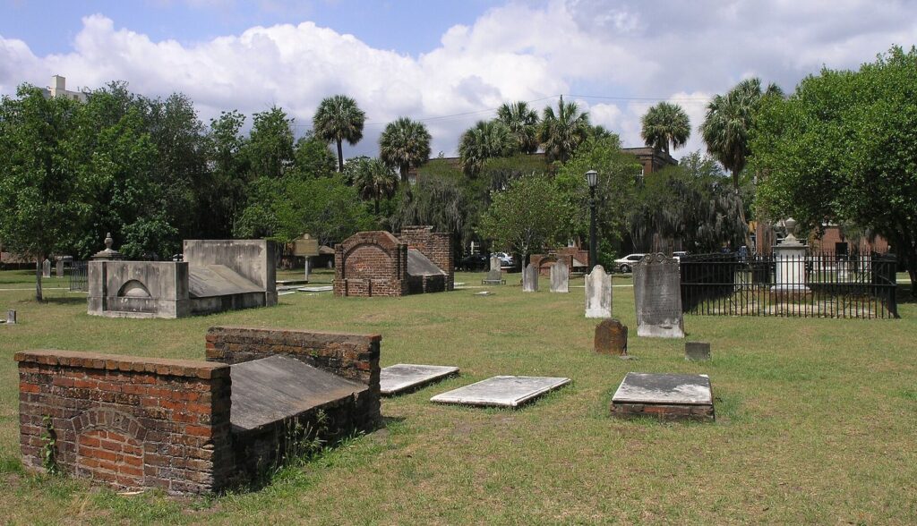 Brick box tombs and weathered headstones on the lawn of Colonial Park Cemetery in Savannah, with palms behind