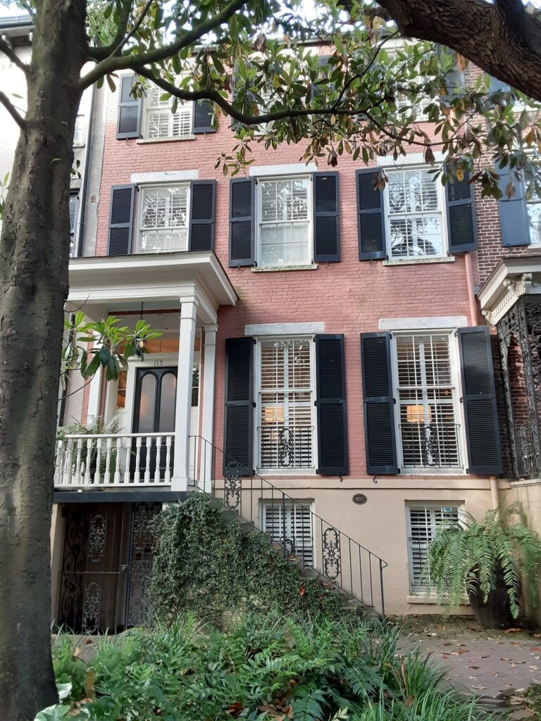 A pink brick townhouse with dark shutters, a raised stoop and an iron balcony on East Jones Street, Savannah