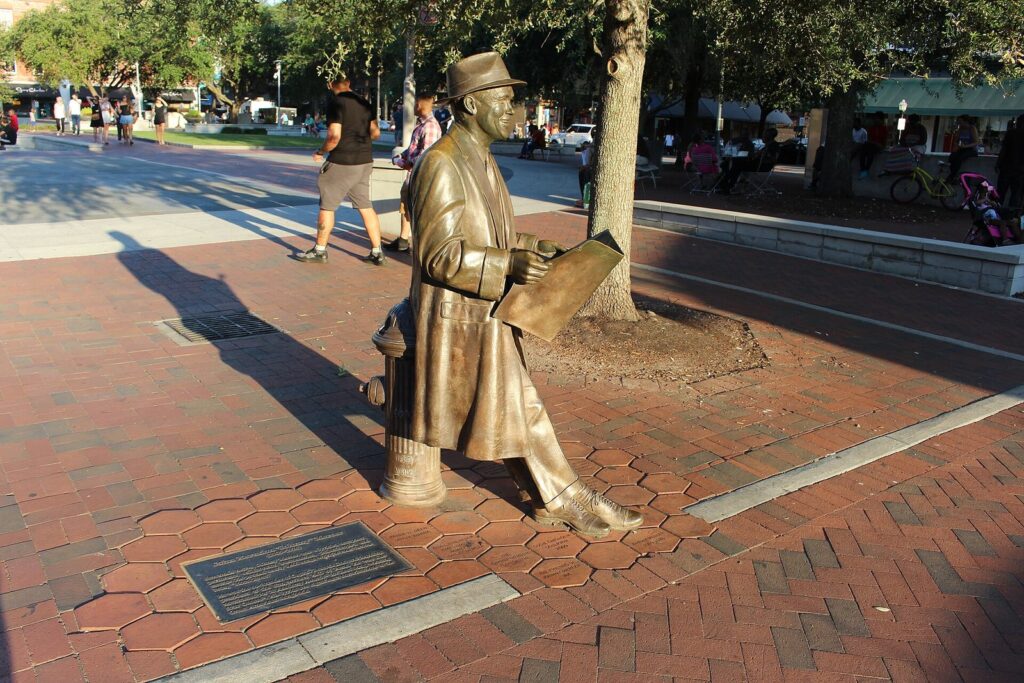 A bronze statue of songwriter Johnny Mercer standing on the brick paving of Ellis Square in Savannah