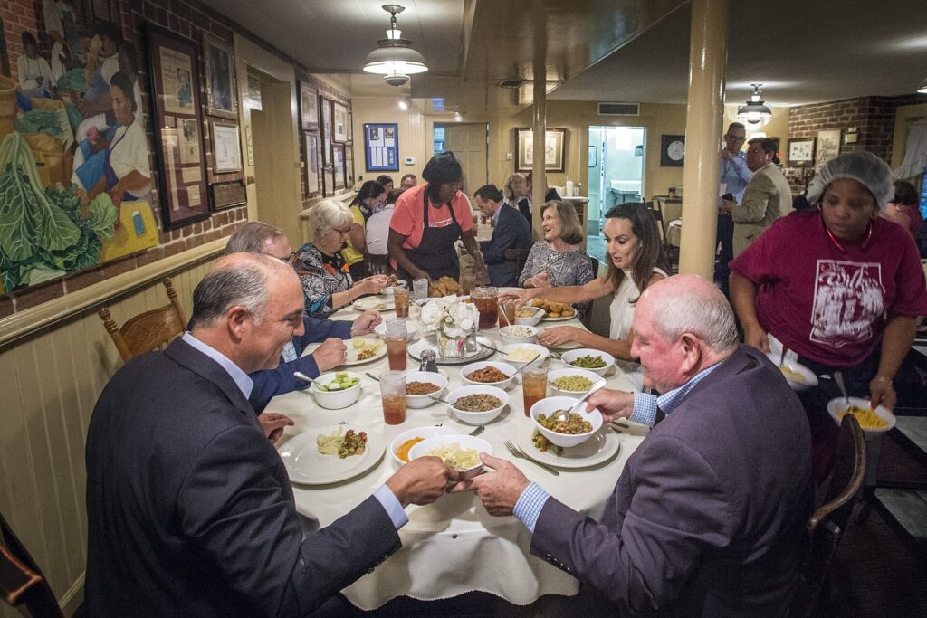 Diners passing bowls of Southern side dishes around a shared table at Mrs. Wilkes' Dining Room in Savannah