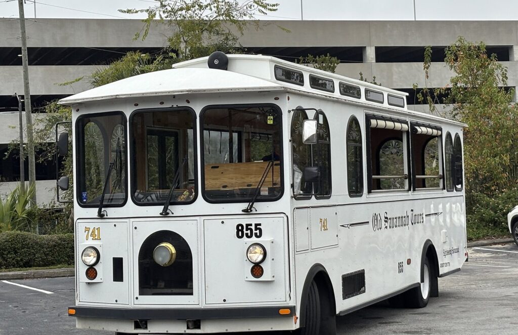 A white Old Savannah Tours trolley bus with arched windows parked in Savannah