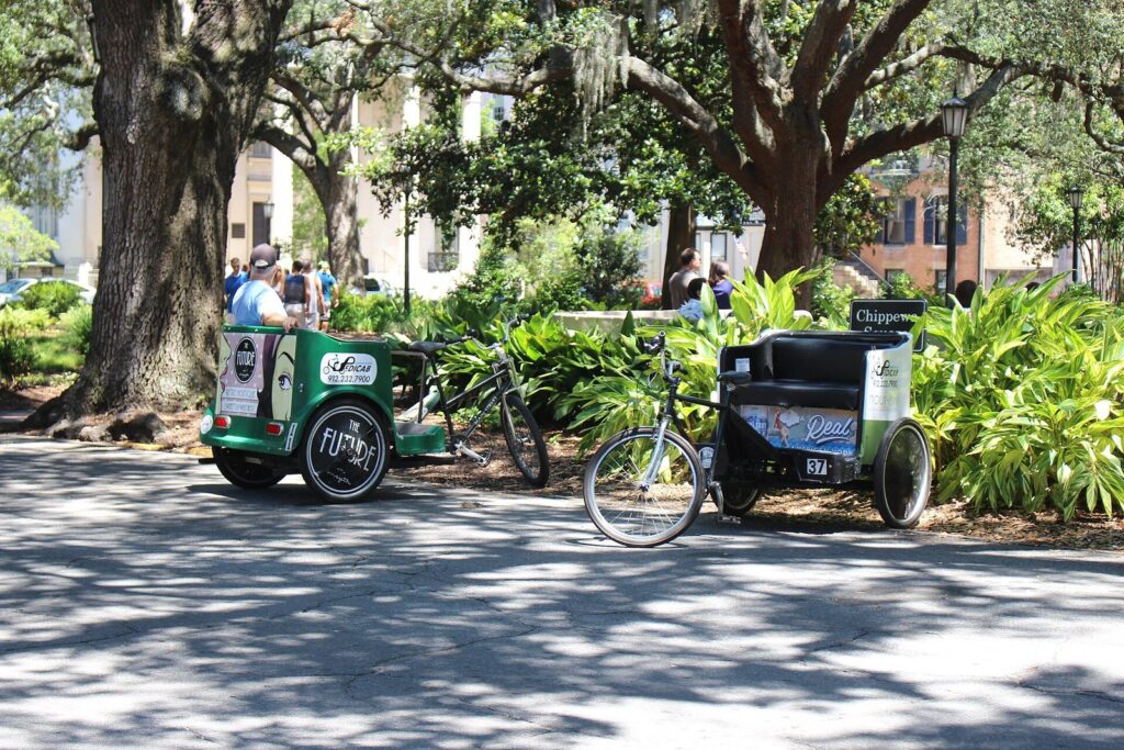 Two pedicabs parked under live oaks at the edge of Chippewa Square in Savannah