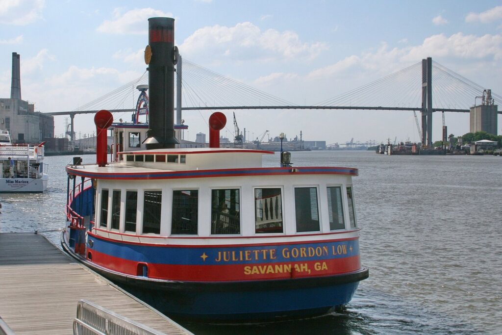 Do you need a car in Savannah? A Savannah Belles Ferry boat docked on the river with the Talmadge Memorial Bridge behind