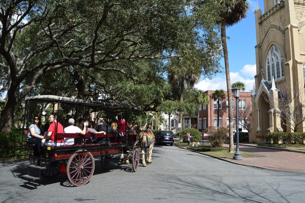 Best Savannah tours compared by interest and budget: a horse-drawn carriage of visitors passing a church and live oaks on a Savannah square