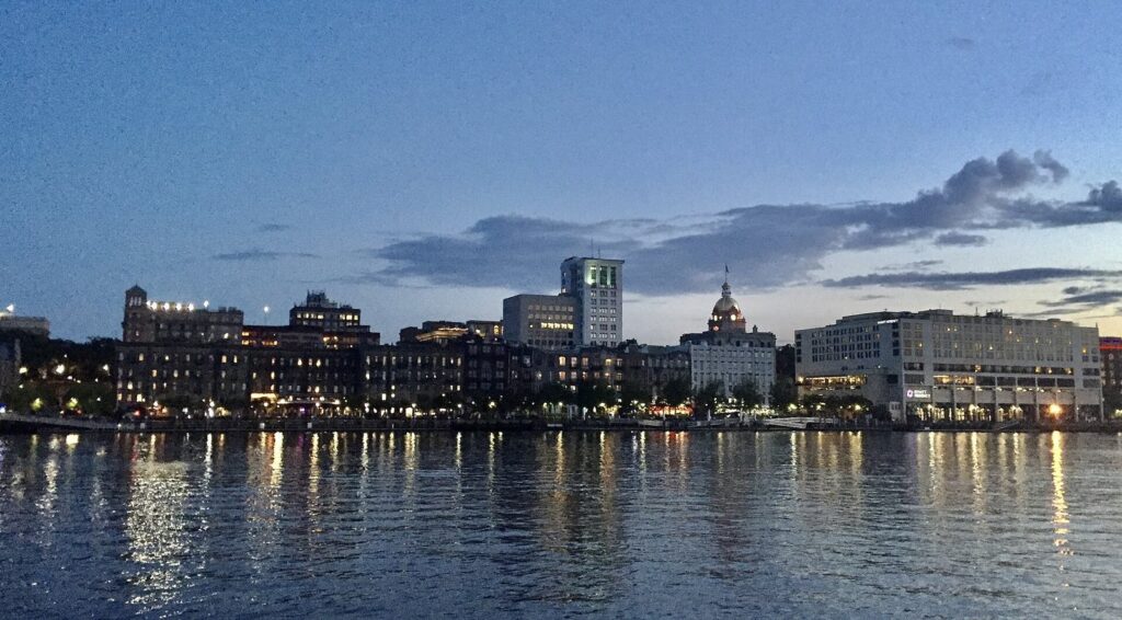 Savannah's riverfront skyline at dusk, with lights reflected in the river and City Hall's dome among the buildings